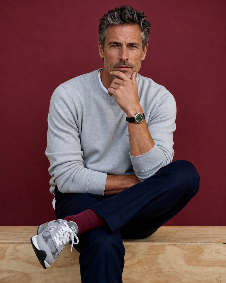 Man in his late 40s wearing Democratique Originals Fine Rib socks in Bordeaux, sitting relaxed in a grey sweater and navy chinos