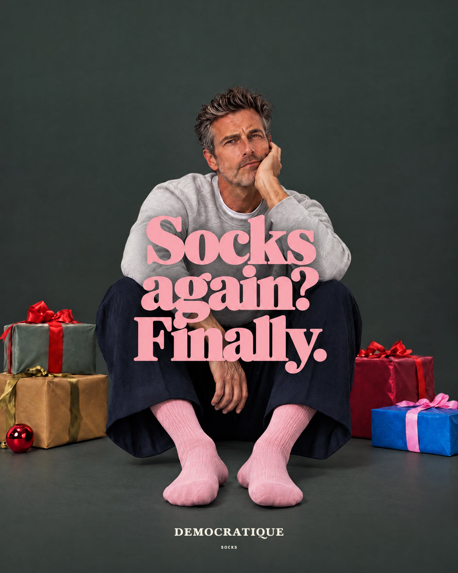 Man in pale pink ribbed socks sitting among wrapped Christmas presents – Democratique Socks campaign: Socks again? Finally.